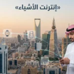 غلاف فوتوغرافي لمدينة سعودية حديثة ورجل يستخدم هاتفاً ذكياً مع رموز متصلة ترمز إلى إنترنت الأشياء (Internet of Things - IoT).