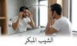 شاب عربي في العشرينيات ينظر في المرآة ويلاحظ ظهور الشيب المبكر على صدغيه