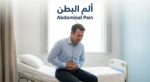 شخص بالغ يجلس على حافة سرير ويمسك بطنه بتعبير ألم خفيف مع نص ألم البطن