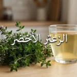 حزمة من أغصان الزعتر الأخضر الطازج بأوراقه الصغيرة وأزهاره الأرجوانية موضوعة على سطح خشبي بجانب كوب منقوع الزعتر الذهبي