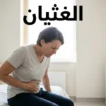 امرأة بالغة تجلس على حافة سرير وتضع يدها على بطنها مع تعبير وجه يدل على الشعور بالغثيان