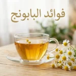 كوب شاي بابونج ذهبي اللون بجانب أزهار البابونج الطازجة على سطح خشبي مع عبارة فوائد البابونج