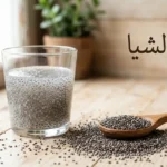 بذور الشيا مبعثرة على سطح خشبي مع ملعقة خشبية وكوب يحتوي على بذور الشيا المنقوعة المتحولة إلى مادة هلامية