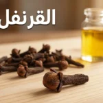 حفنة من مسامير القرنفل المجففة ذات اللون البني الداكن على سطح خشبي مع زجاجة زيت القرنفل في الخلفية وعنوان القرنفل بالعربية