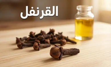 حفنة من مسامير القرنفل المجففة ذات اللون البني الداكن على سطح خشبي مع زجاجة زيت القرنفل في الخلفية وعنوان القرنفل بالعربية