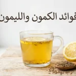 كوب زجاجي يحتوي على مشروب الكمون والليمون الذهبي الدافئ مع نصف ليمونة وبذور كمون على ملعقة خشبية وخلفية بيضاء نظيفة