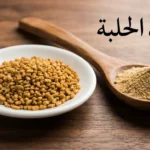 حفنة من بذور الحلبة الذهبية على طبق خزفي أبيض بجانب ملعقة خشبية تحتوي مسحوق الحلبة على سطح خشبي مع نص فوائد الحلبة