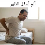 رجل يجلس على حافة سريره ويضع يده على أسفل ظهره بتعبير يدل على الألم