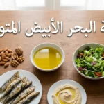مائدة طعام متوسطية تحتوي على زيت زيتون وسلطة خضراء وحمص وسمك مشوي ومكسرات مع عبارة حمية البحر الأبيض المتوسط