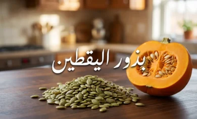 حفنة من بذور اليقطين الخضراء النيئة على سطح خشبي بجوار نصف ثمرة يقطين مفتوحة مع نص عربي يقول بذور اليقطين