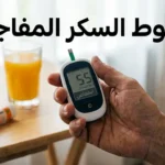 يد تمسك جهاز قياس سكر الدم يعرض قراءة منخفضة مع كوب عصير برتقال وأقراص جلوكوز في الخلفية وعبارة هبوط السكر المفاجئ