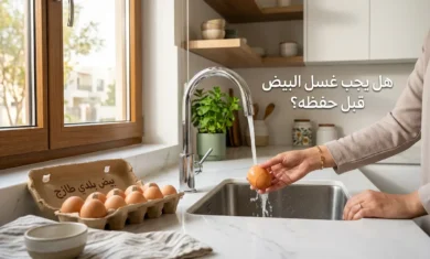 يد امرأة تغسل بيضة تحت صنبور ماء في مطبخ عربي حديث مع نص "هل يجب غسل البيض قبل حفظه؟